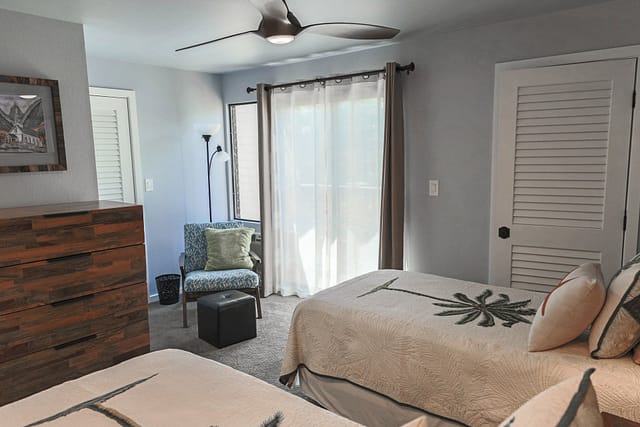 Low height ceiling fan with 2 twin beds, tall wood dresser and lounge chair.